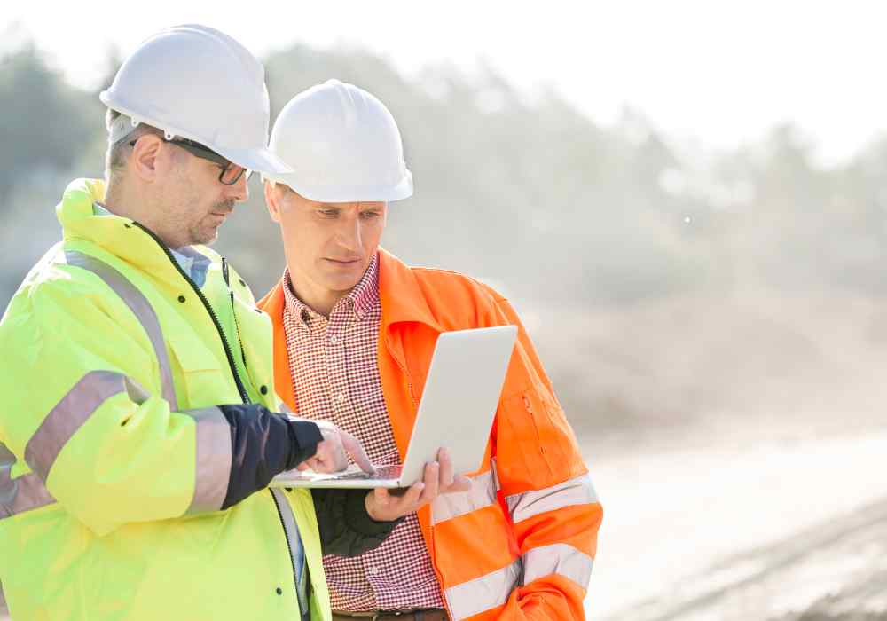 Two engineers in hard hats reviewing site data on a tablet